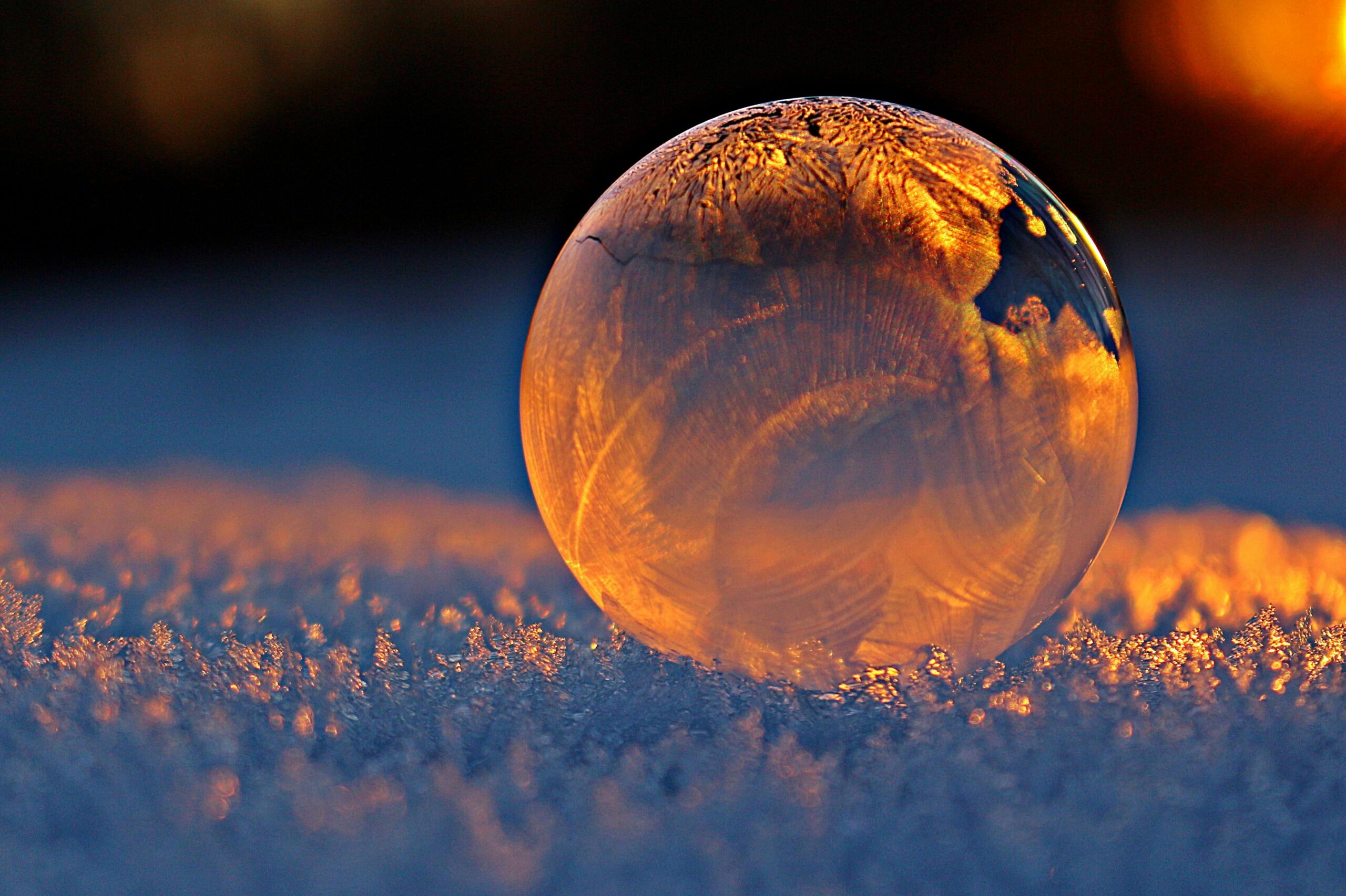 About Close-up shot of a frozen bubble with warm reflections resting on a snowy surface at twilight.